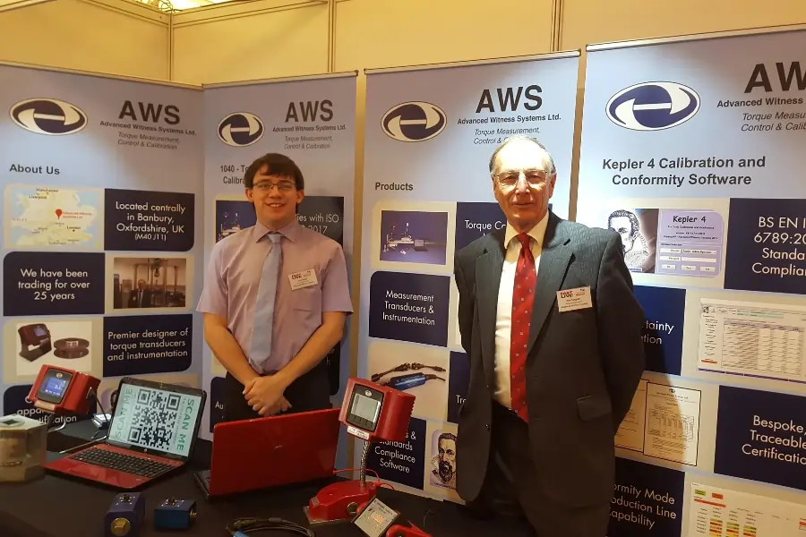 Two men stood at an exhibition stand with torque calibration and verification equipment