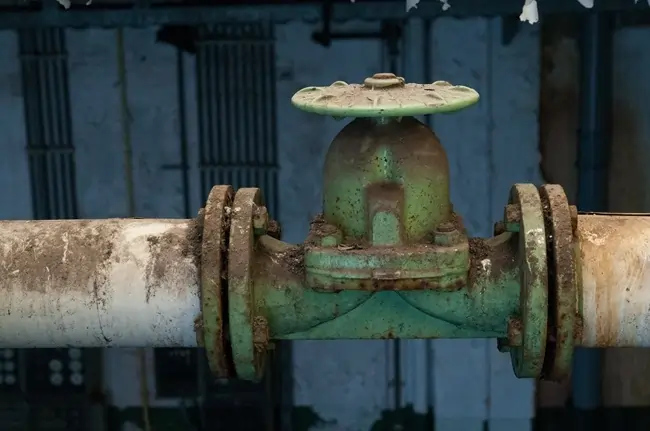 A muddy, rusty pipe bolting into an oil and gas rig setup
